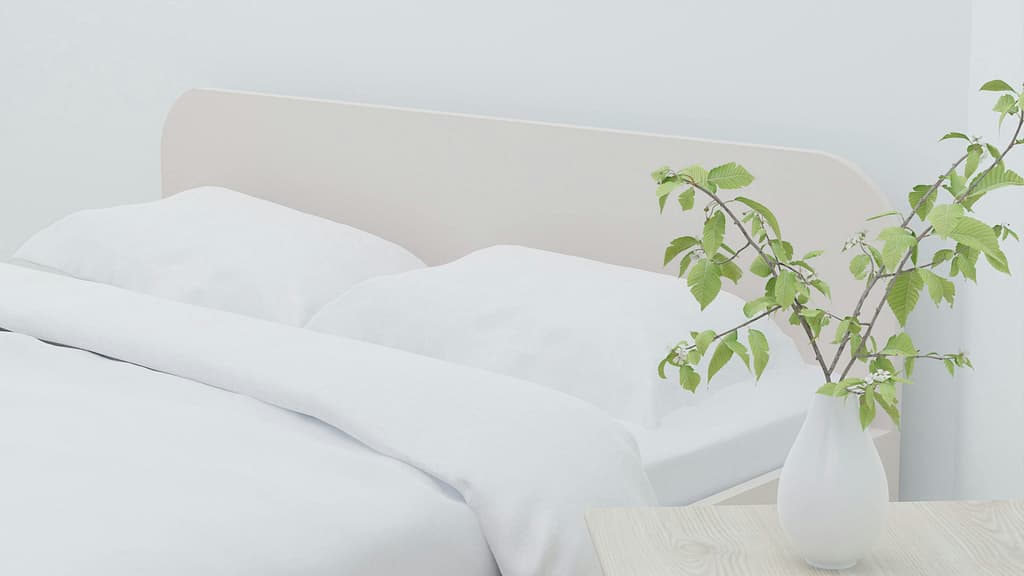 Light and airy modern bedroom with white bedding and a vase of greenery on a wooden table.