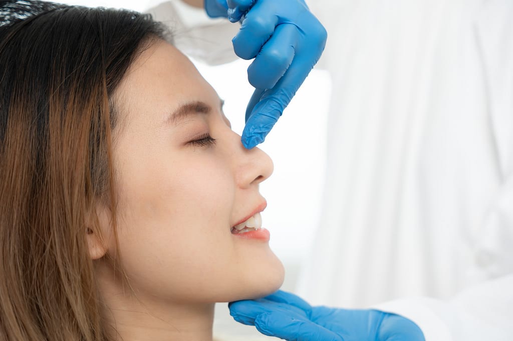 A plastic surgeon evaluating a female patient's nose profile during a rhinoplasty consultation in Ho Chi Minh City.