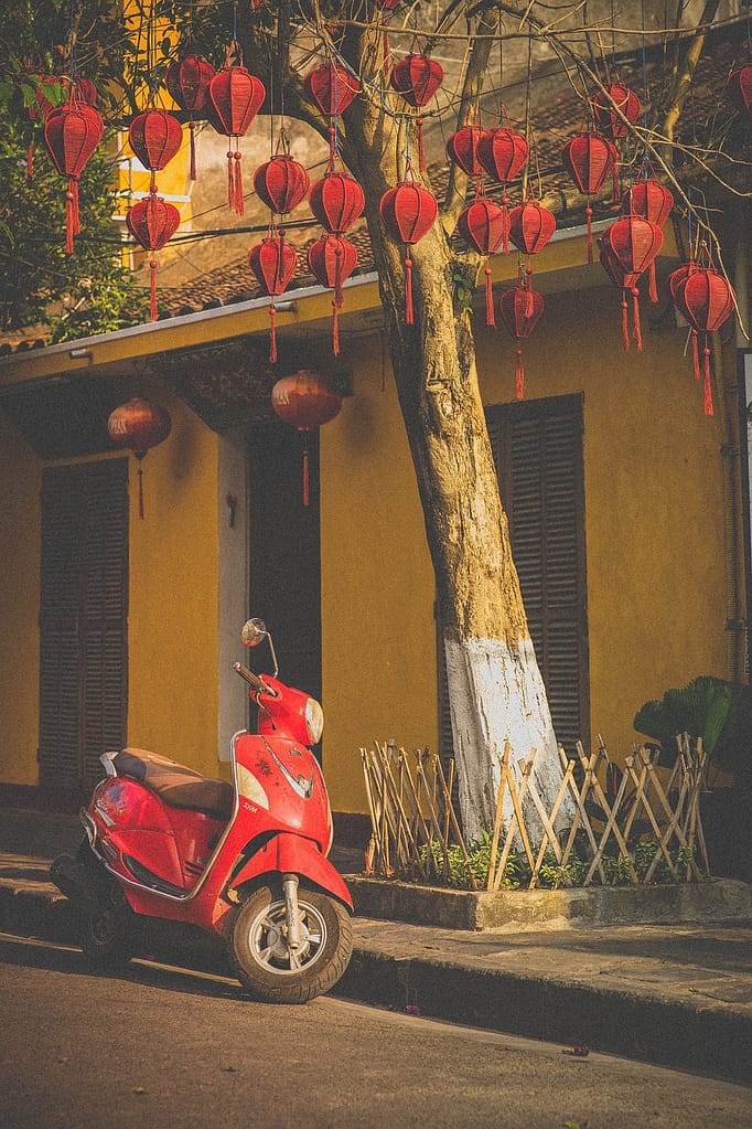 A classic red motorbike parked in front of traditional red lanterns in Hoi An, capturing the cultural charm of Vietnam for luxury medical travelers.