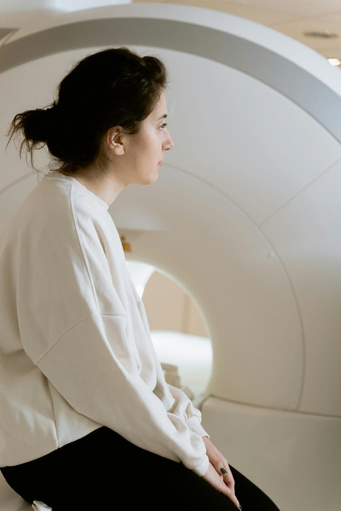 A woman seated near a CT scanner, capturing a medical and clinical environment.